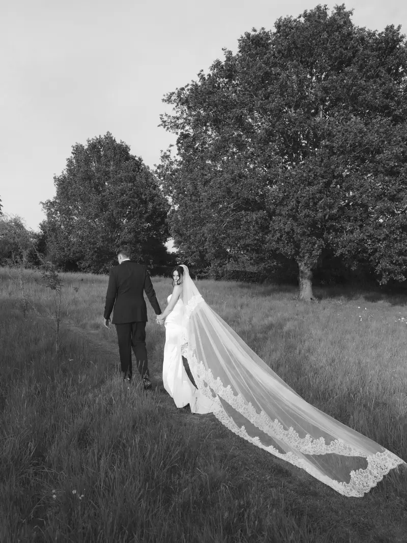 A bride walking with a long veil across a field