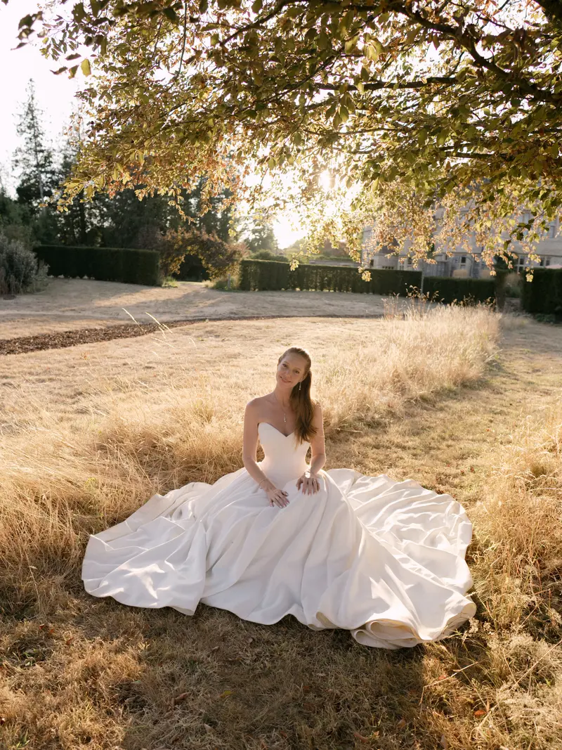 A bride sitting in her gown in a golden field at sunset