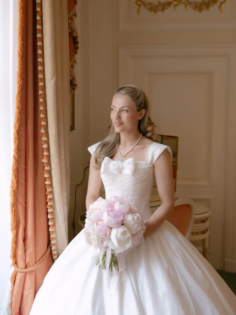 A bride holding peonies by a window
